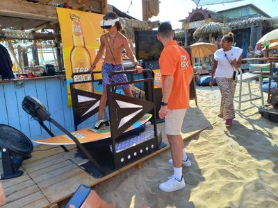 Participant debout sur la planche de surf dynamique avec casque VR sur une plage